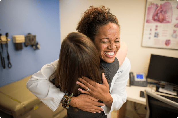 A female medical staff member smiles as she hugs a young female patient.