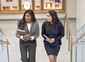 Two female NYU Grossman School of Medicine staff members carry books and walk upstairs together.