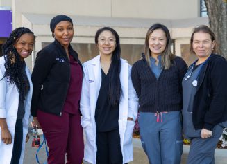 Five female NYU Langone Hospital—Brooklyn staff members stand together smiling for a photo outside the hospital.