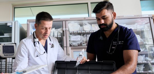 Two male NYU Langone Hospital—Long Island medical staff members check medical stock together.