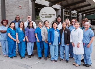 A diverse group of NYU Langone Orthopedic Hospital staff pose for a photo outside the hospital.