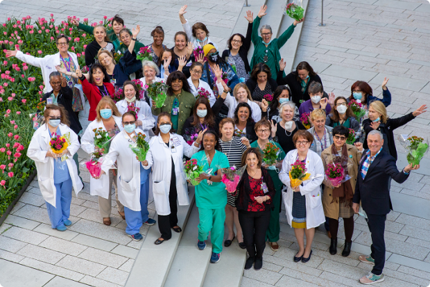 A large group of staff members in an outdoor setting wave and smile for an overhead camera photo op.