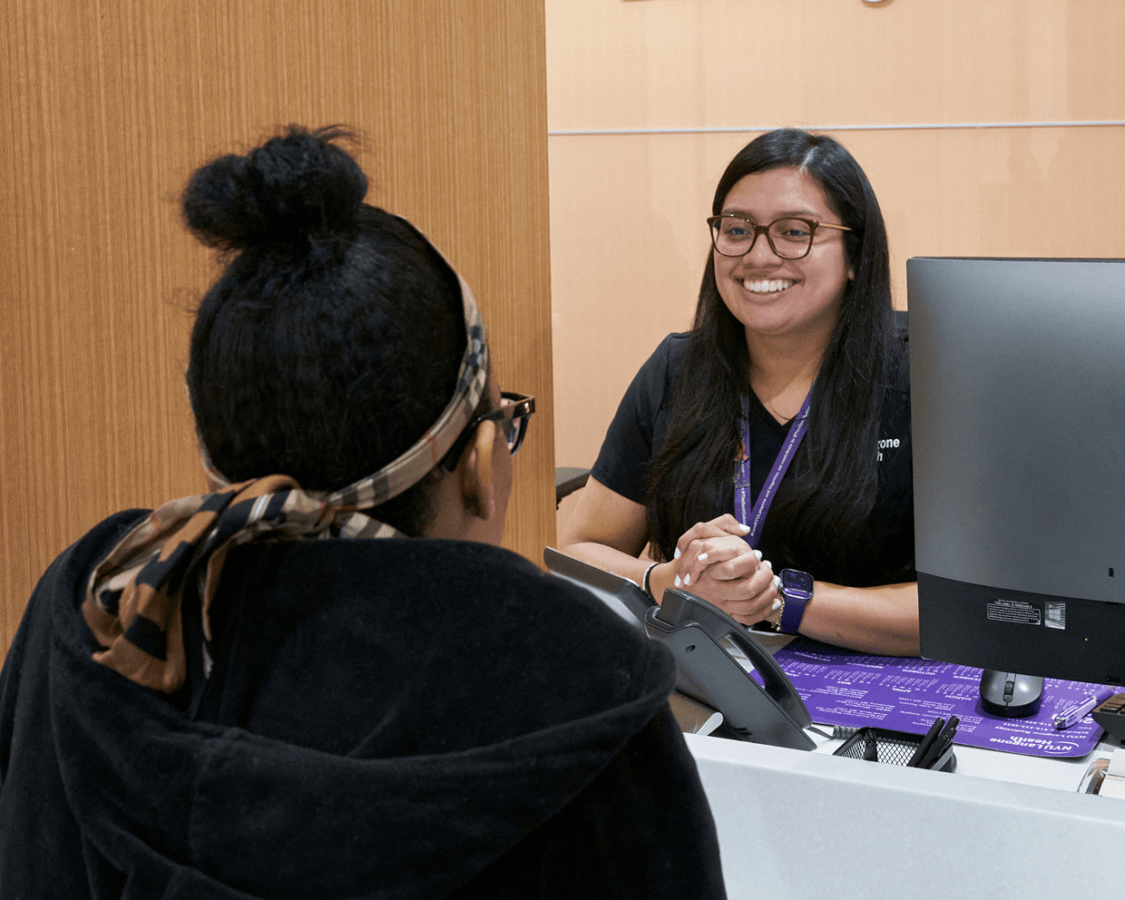 Two female medical support staff at NYU Langone talk together while working at their desks.