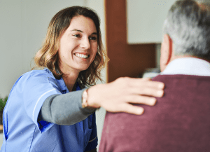 A smiling healthcare professional places a comforting hand on the shoulder of an older man